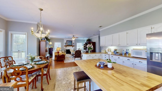 dining space featuring ceiling fan with notable chandelier, a healthy amount of sunlight, crown molding, and light hardwood / wood-style floors