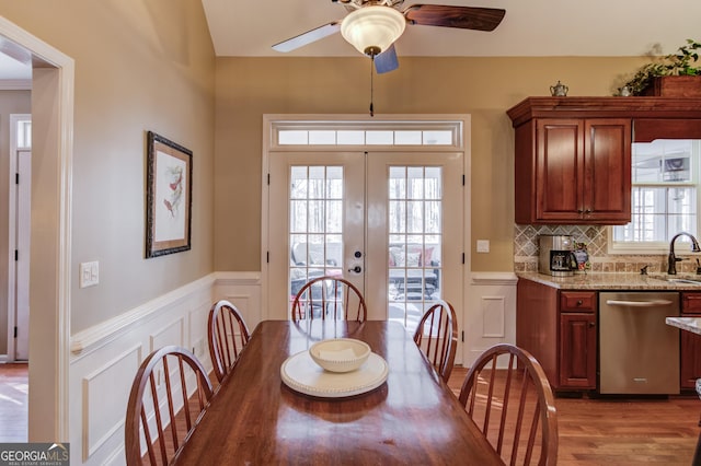 dining room featuring french doors, a decorative wall, wood finished floors, and wainscoting