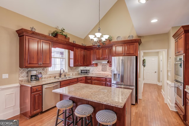 kitchen with light wood-style floors, appliances with stainless steel finishes, a center island, under cabinet range hood, and a sink