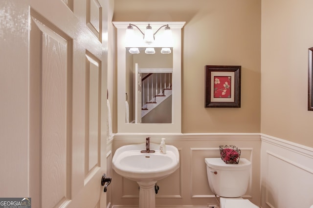 half bathroom featuring a wainscoted wall, a sink, toilet, and a decorative wall