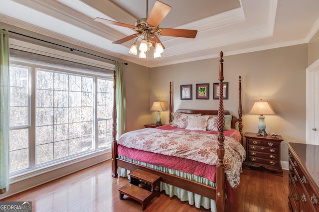 bedroom with ornamental molding, a tray ceiling, multiple windows, and wood finished floors