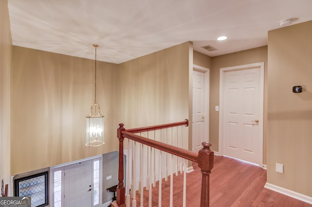 corridor with baseboards, visible vents, wood finished floors, an upstairs landing, and a notable chandelier