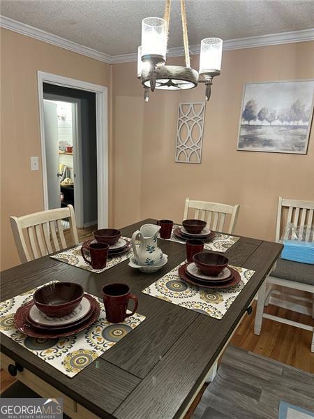 dining area featuring a textured ceiling, ornamental molding, a chandelier, and dark hardwood / wood-style flooring