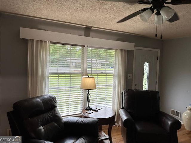 living area featuring ceiling fan, wood-type flooring, and a textured ceiling