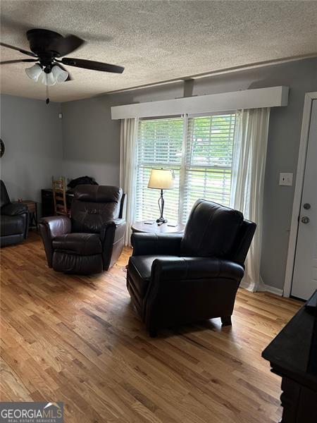 living room with hardwood / wood-style flooring, ceiling fan, and a textured ceiling