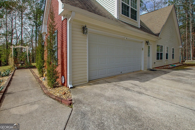 view of side of property with brick siding, a shingled roof, and concrete driveway