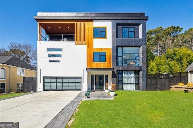 contemporary house with an attached garage, fence, a front yard, stucco siding, and driveway