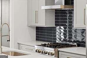 kitchen with stove, stainless steel gas cooktop, decorative backsplash, sink, and white cabinetry