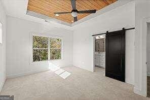 unfurnished bedroom featuring a tray ceiling, wooden ceiling, a barn door, and carpet floors