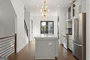 kitchen featuring premium appliances, decorative light fixtures, sink, white cabinetry, and a kitchen island with sink