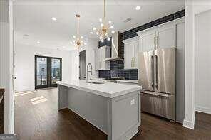 kitchen featuring white cabinetry, pendant lighting, wall chimney range hood, stainless steel appliances, and an island with sink