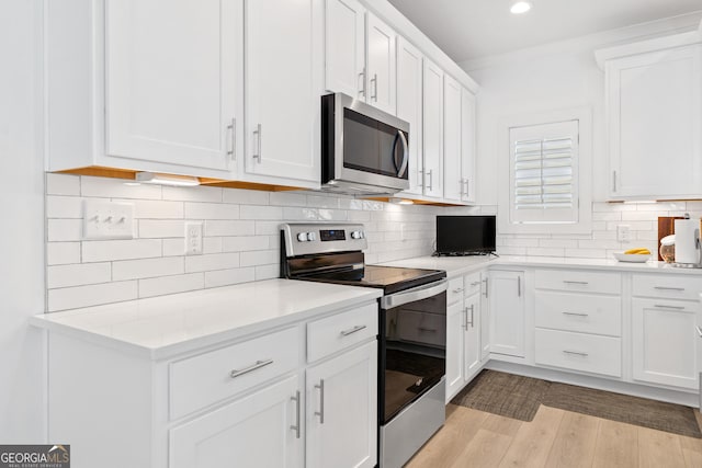 kitchen with tasteful backsplash, stainless steel appliances, white cabinetry, and light hardwood / wood-style floors