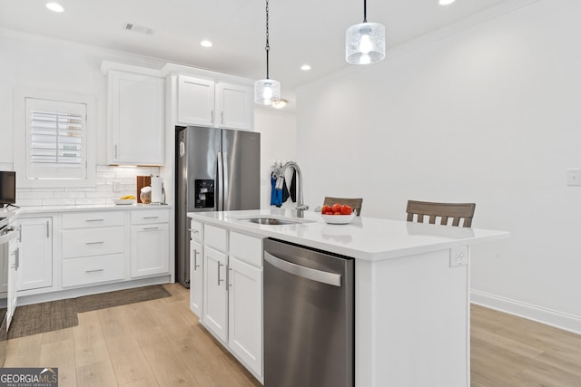 kitchen with an island with sink, white cabinetry, stainless steel appliances, and decorative light fixtures