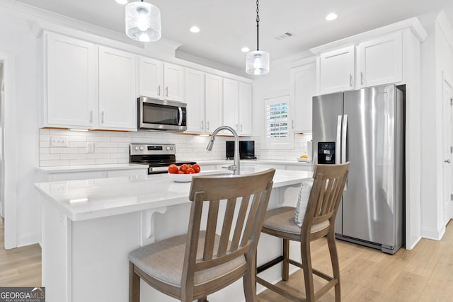 kitchen with a center island with sink, appliances with stainless steel finishes, white cabinets, and decorative light fixtures