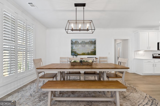 dining area with light wood-type flooring, crown molding, and an inviting chandelier