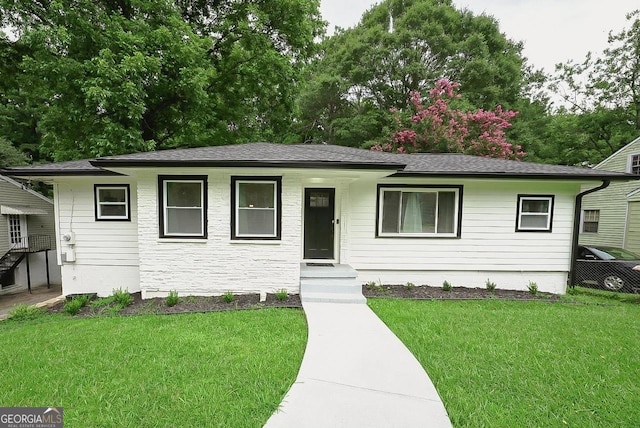 ranch-style home with a shingled roof and a front lawn