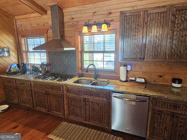 kitchen with appliances with stainless steel finishes, sink, stone countertops, wood walls, and wall chimney exhaust hood