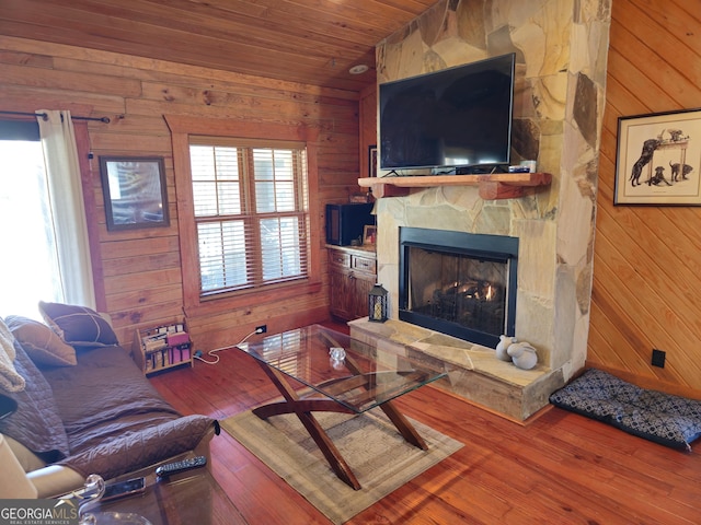 living room with a stone fireplace, wood ceiling, hardwood / wood-style floors, and wooden walls