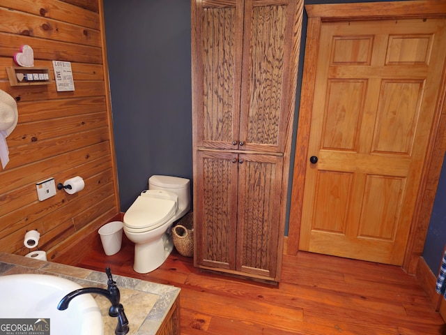 bathroom with toilet, hardwood / wood-style flooring, and wood walls