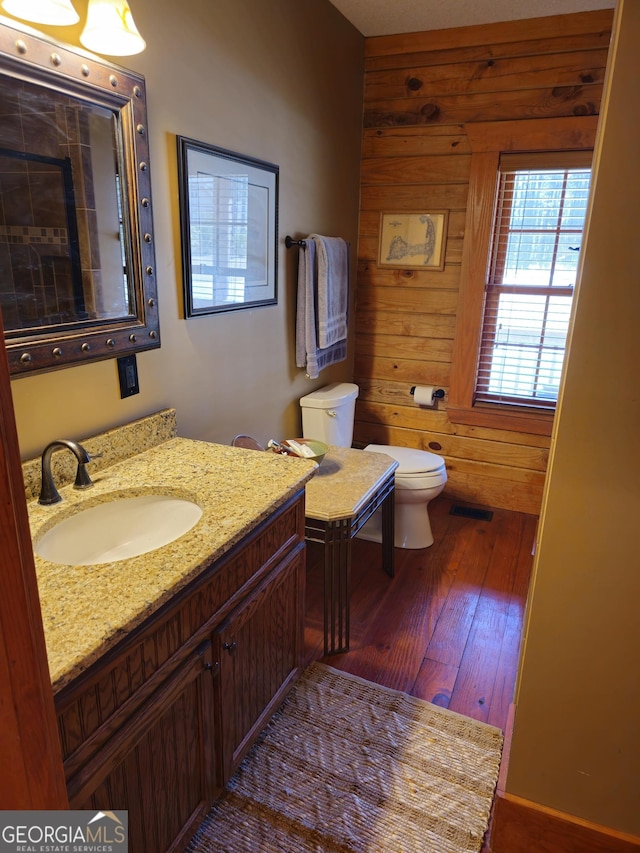 bathroom with toilet, vanity, hardwood / wood-style floors, and wooden walls