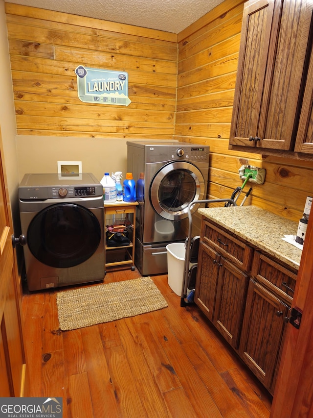 washroom with cabinets, dark hardwood / wood-style flooring, wood walls, washing machine and clothes dryer, and a textured ceiling