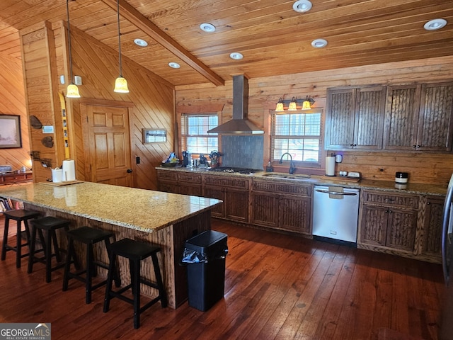 kitchen featuring appliances with stainless steel finishes, wall chimney exhaust hood, light stone countertops, decorative light fixtures, and a kitchen island