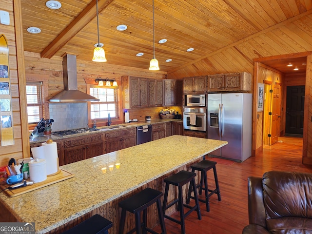 kitchen featuring wall chimney range hood, hanging light fixtures, stainless steel appliances, and wood walls