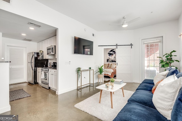 living room with concrete flooring, ceiling fan, and a barn door