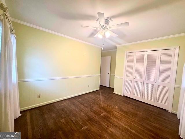 unfurnished bedroom featuring baseboards, dark wood finished floors, a ceiling fan, and crown molding