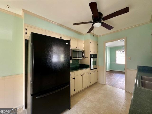 kitchen with dark countertops, appliances with stainless steel finishes, crown molding, and wainscoting