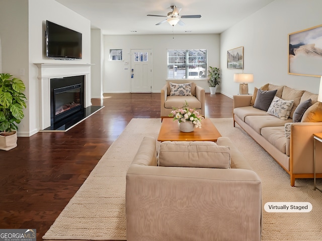 living area with ceiling fan, wood finished floors, a glass covered fireplace, and baseboards