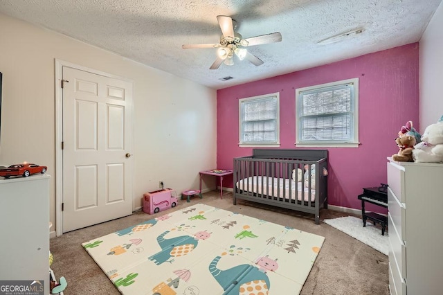 bedroom featuring a crib, a textured ceiling, carpet, and ceiling fan