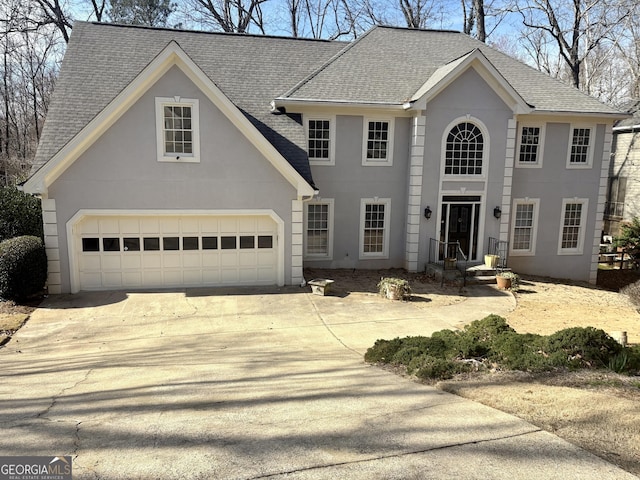 colonial home featuring a shingled roof, concrete driveway, a garage, and stucco siding