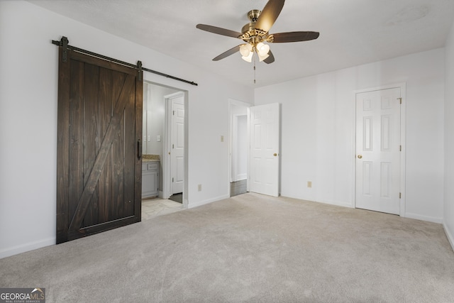 unfurnished bedroom featuring a barn door, connected bathroom, light colored carpet, a ceiling fan, and baseboards