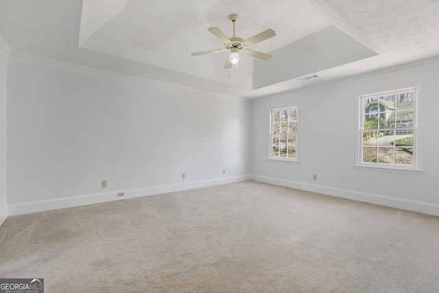 carpeted empty room with baseboards, visible vents, ceiling fan, ornamental molding, and a tray ceiling