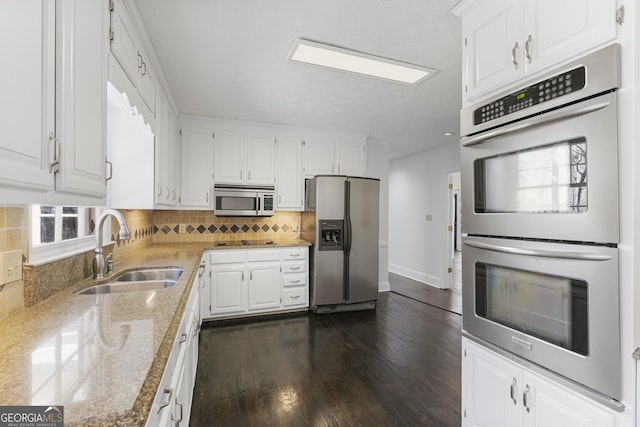 kitchen featuring stainless steel appliances, a sink, white cabinets, light stone countertops, and tasteful backsplash