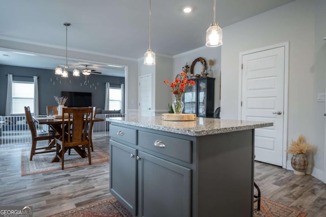 kitchen featuring hardwood / wood-style floors, gray cabinets, a center island, hanging light fixtures, and light stone countertops