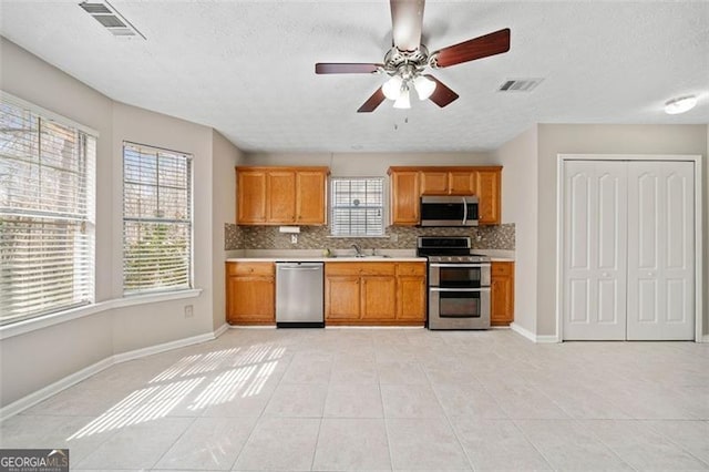 kitchen with a textured ceiling, stainless steel appliances, decorative backsplash, and light tile patterned floors