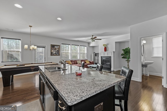 kitchen with dark wood-style floors, light stone counters, a glass covered fireplace, a sink, and dishwasher