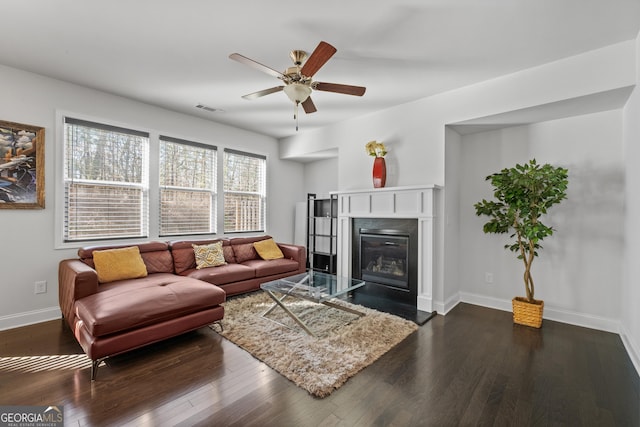 living area featuring baseboards, visible vents, dark wood-style flooring, and a fireplace with flush hearth