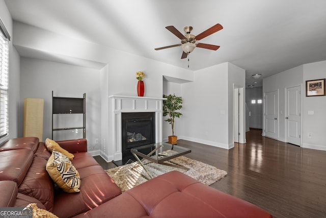 living area featuring ceiling fan, a glass covered fireplace, wood finished floors, and baseboards