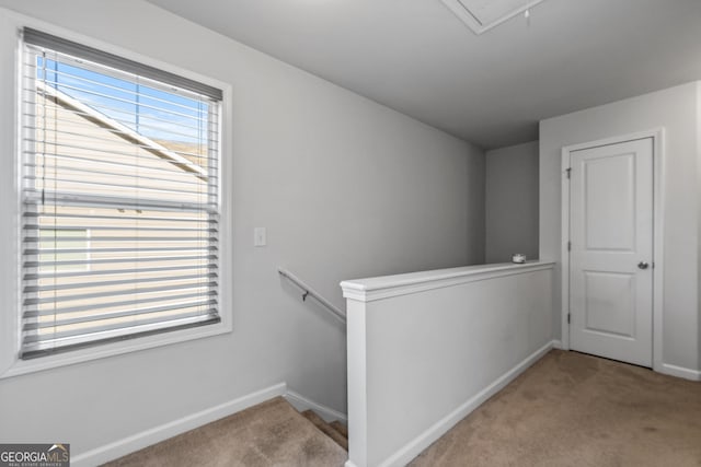 hallway featuring carpet, baseboards, attic access, and an upstairs landing