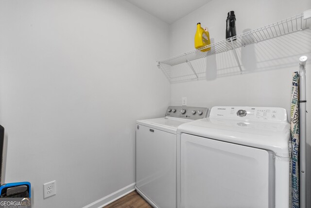 clothes washing area featuring dark wood-style floors, laundry area, washing machine and dryer, and baseboards