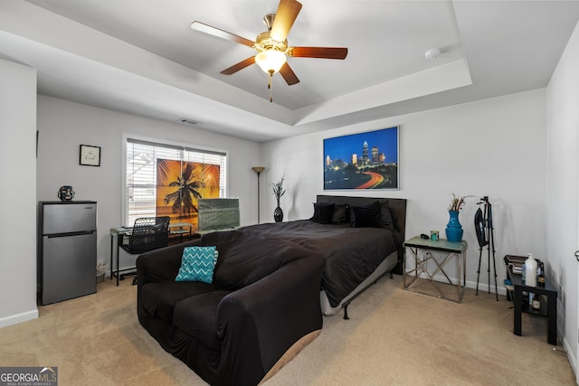 bedroom with light carpet, a tray ceiling, freestanding refrigerator, and baseboards