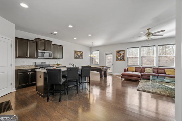 kitchen with a breakfast bar area, recessed lighting, dark wood-style flooring, appliances with stainless steel finishes, and a center island with sink