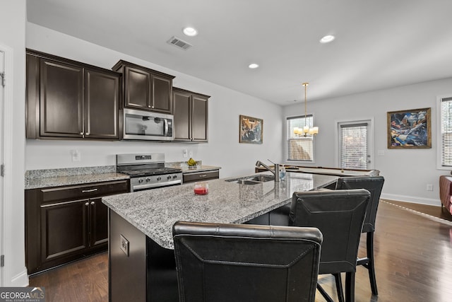 kitchen with light stone counters, dark wood-style flooring, stainless steel appliances, visible vents, and a sink