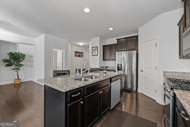 kitchen featuring light stone counters, stainless steel appliances, a sink, dark wood-style floors, and an island with sink