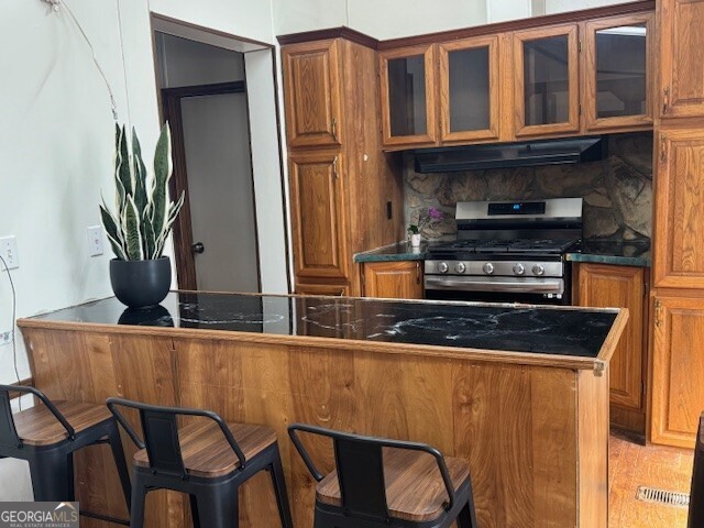 kitchen with brown cabinets, dark countertops, extractor fan, and stainless steel gas stove