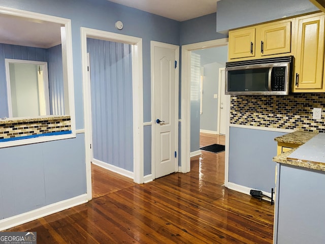 kitchen featuring stainless steel microwave, cream cabinets, decorative backsplash, baseboards, and dark wood-style flooring