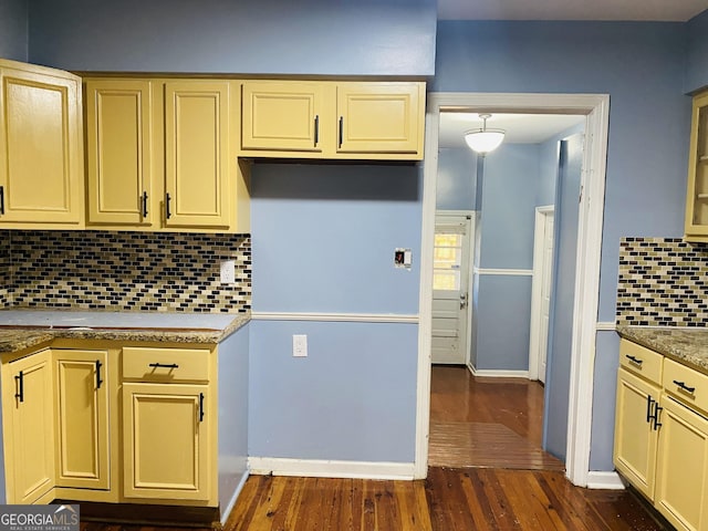 kitchen featuring decorative backsplash, dark wood-type flooring, cream cabinetry, and baseboards